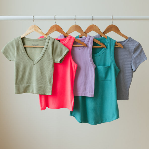 Five bright coloured ribbed tees and tanks on hangers, hung on a clothing rack.