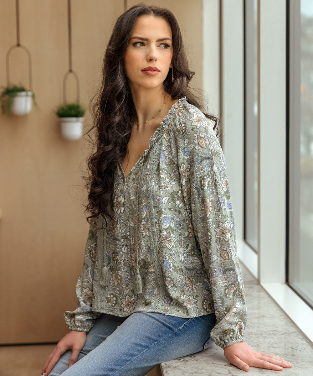 Model staring out a window, wearing a floral long sleeve peasant top paired with medium wash jeans.